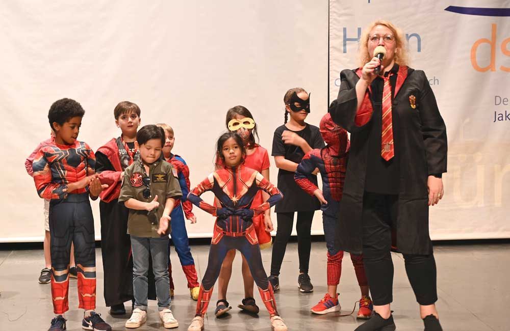A group of children dressed in superhero costumes are standing on a stage.