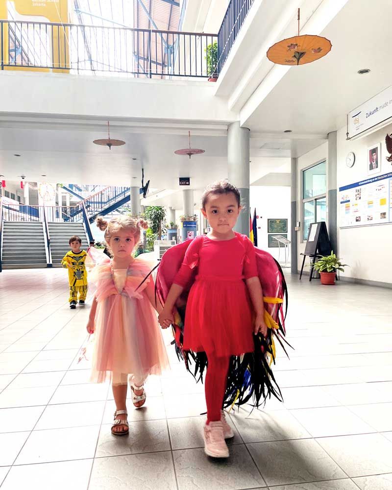 Two little girls are walking down a hallway holding hands.