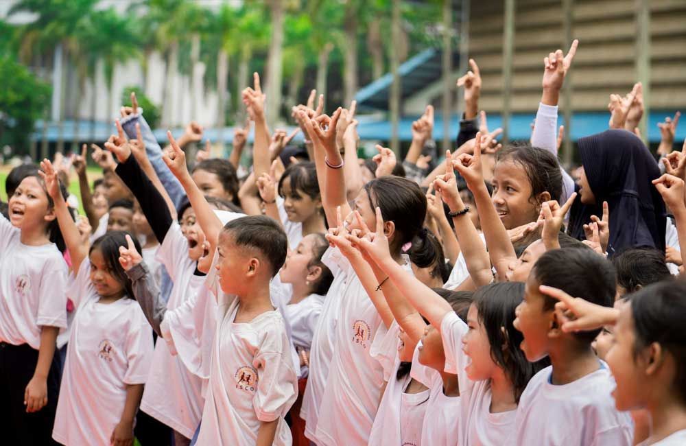 A large group of children are raising their hands in the air.