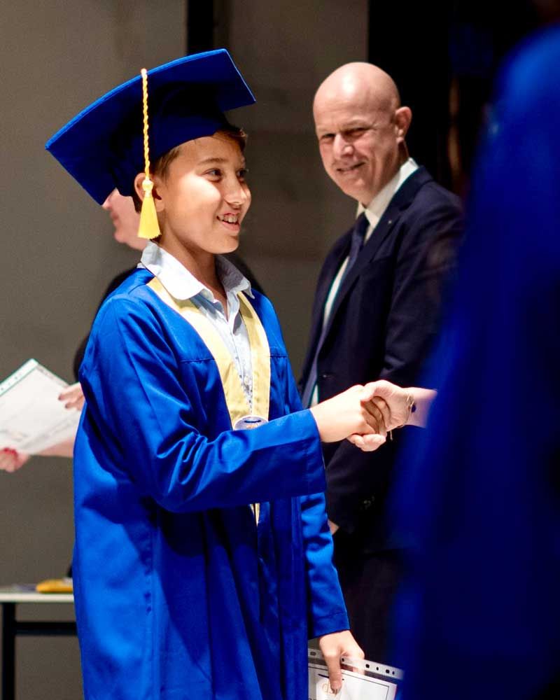 A boy in a graduation cap and gown shakes hands with a man in a suit