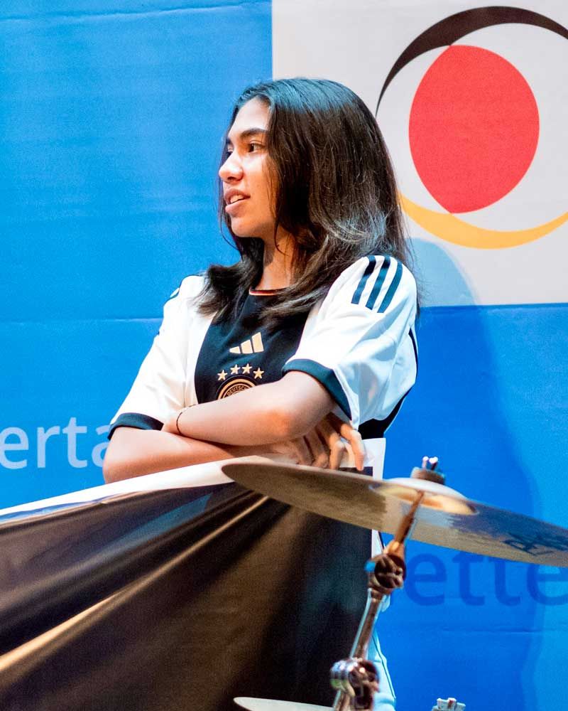 A woman sitting in front of a drum set with the word certo on the wall behind her