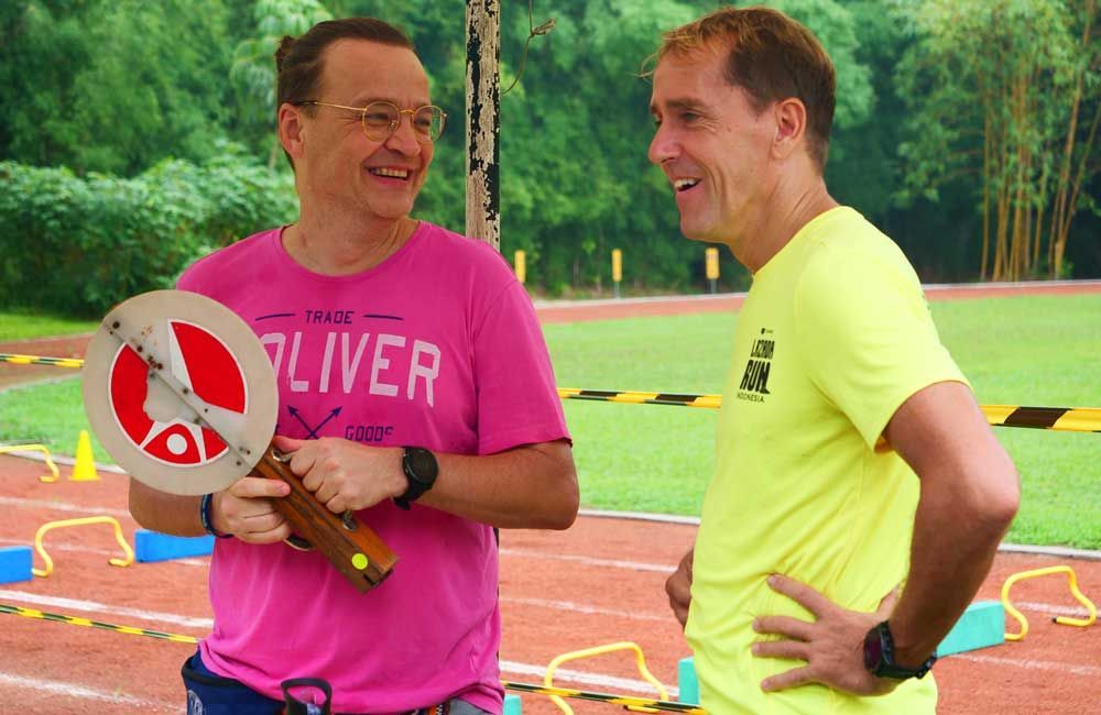 Two men are standing on a track and one of them is wearing a pink shirt that says liver