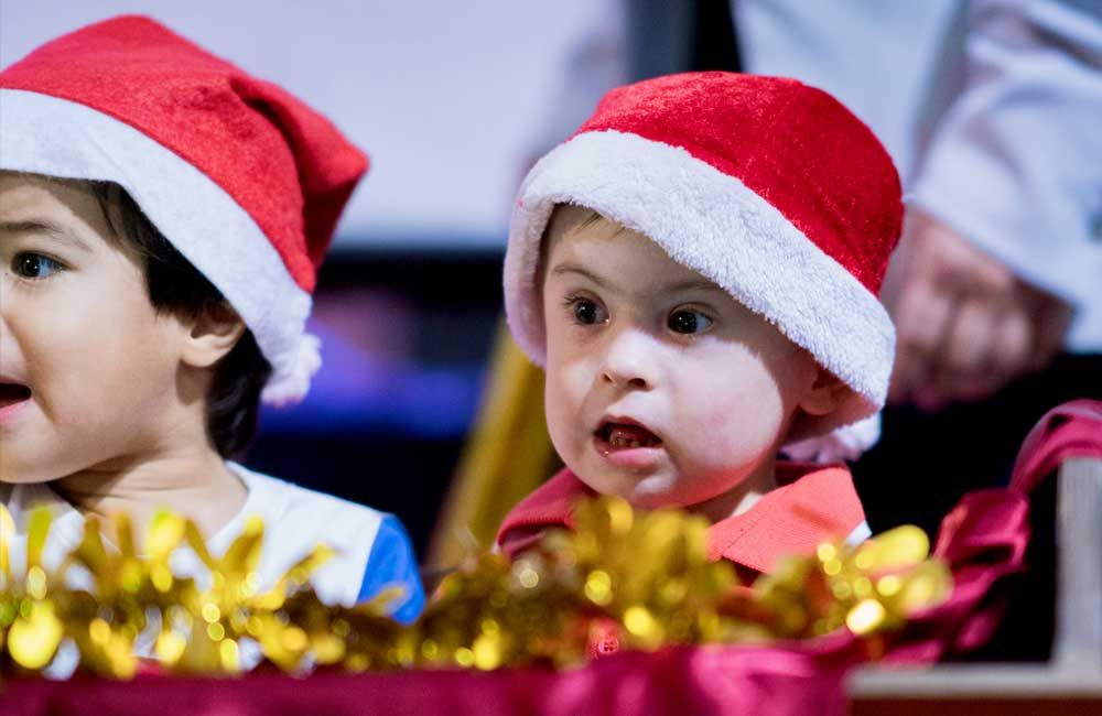 Two children wearing santa hats are sitting next to each other.