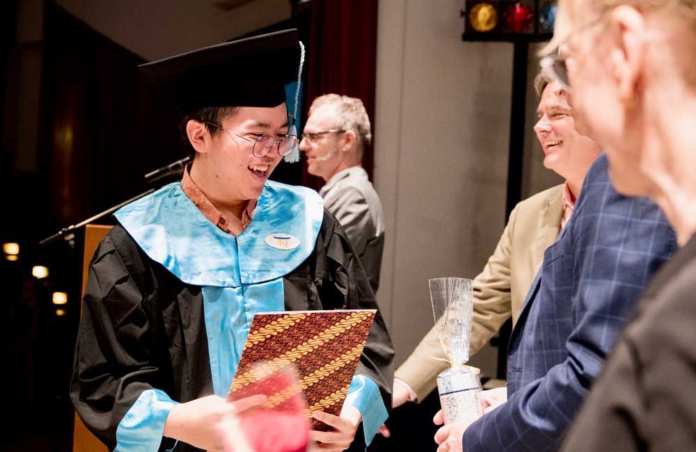 A man in a graduation cap and gown is shaking hands with a group of people.