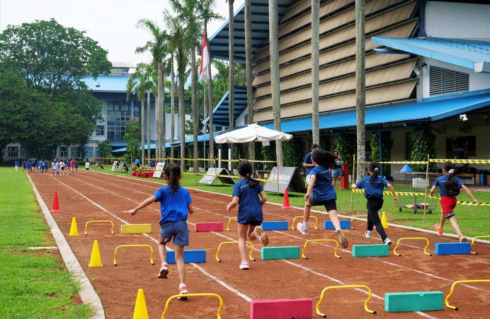 A group of children are running on a track in front of a building.