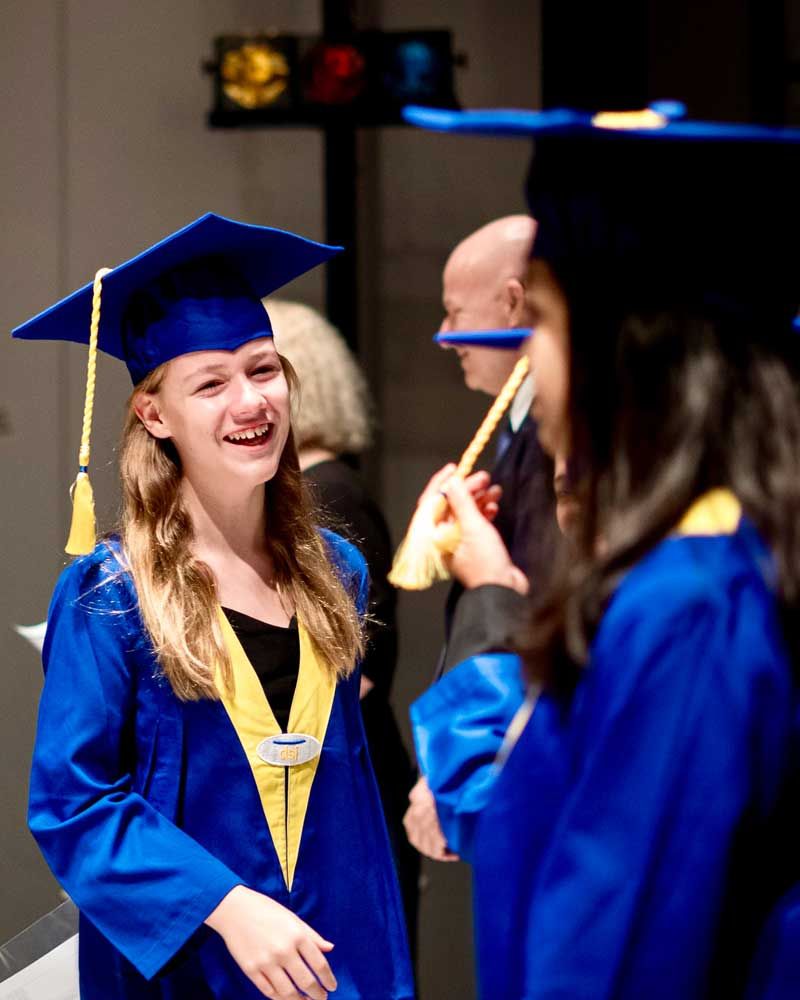 A woman in a graduation cap and gown is smiling while standing next to another woman.