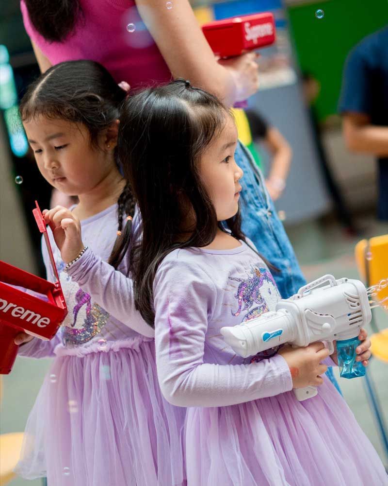 Two little girls are playing with soap bubbles while holding a supreme bag.