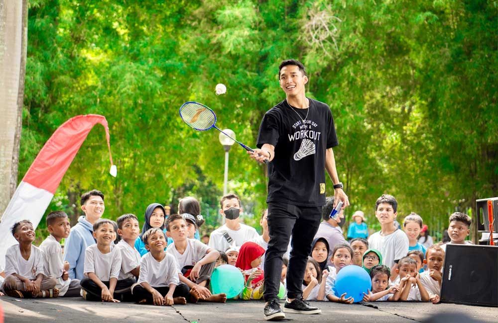 A man is holding a badminton racket in front of a crowd of children.