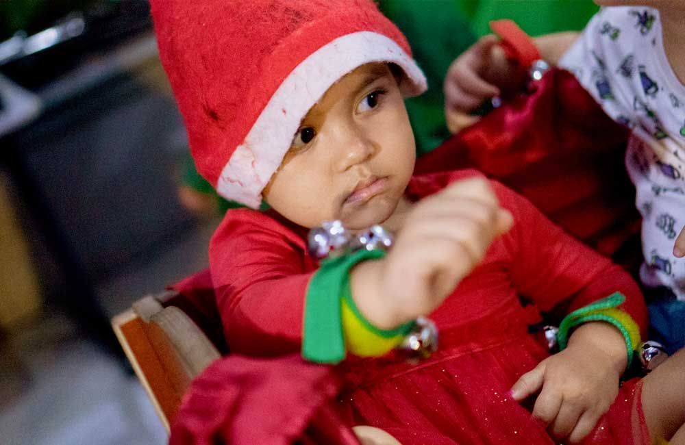 A baby wearing a santa hat and a red dress is sitting in a chair.