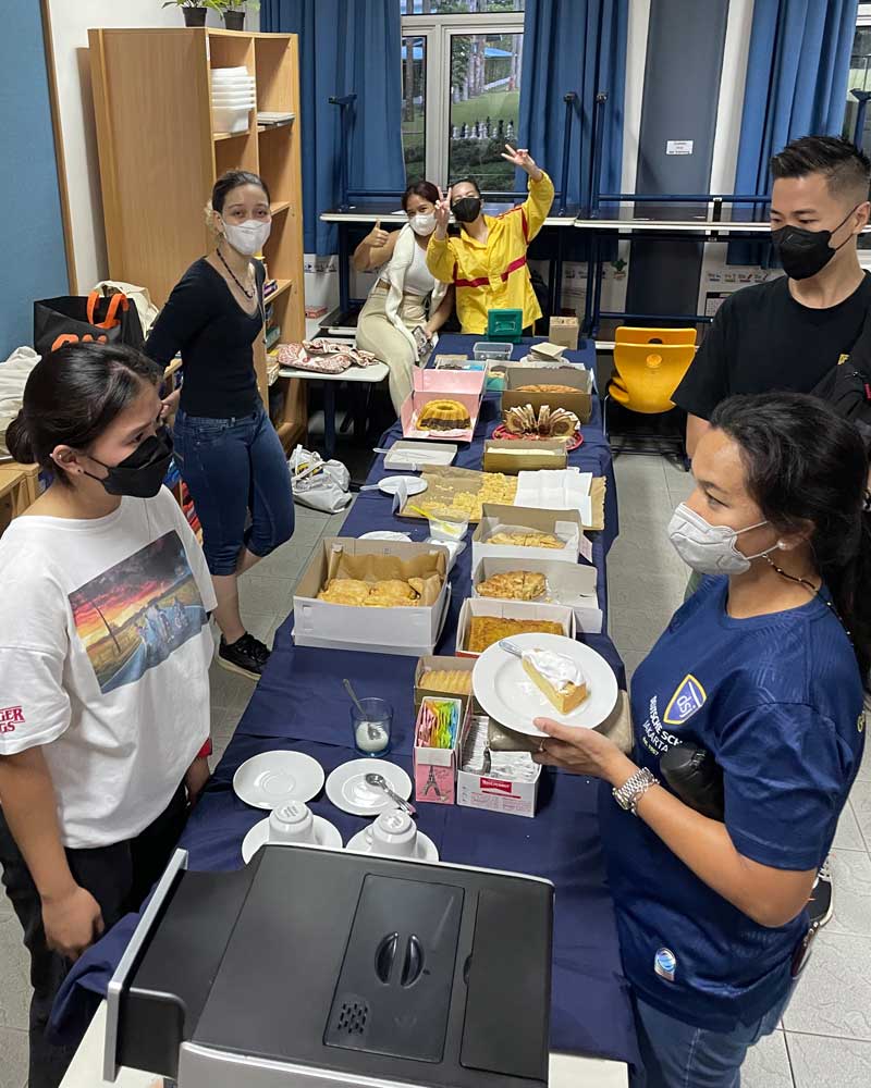 A group of people wearing face masks are standing around a table with food.