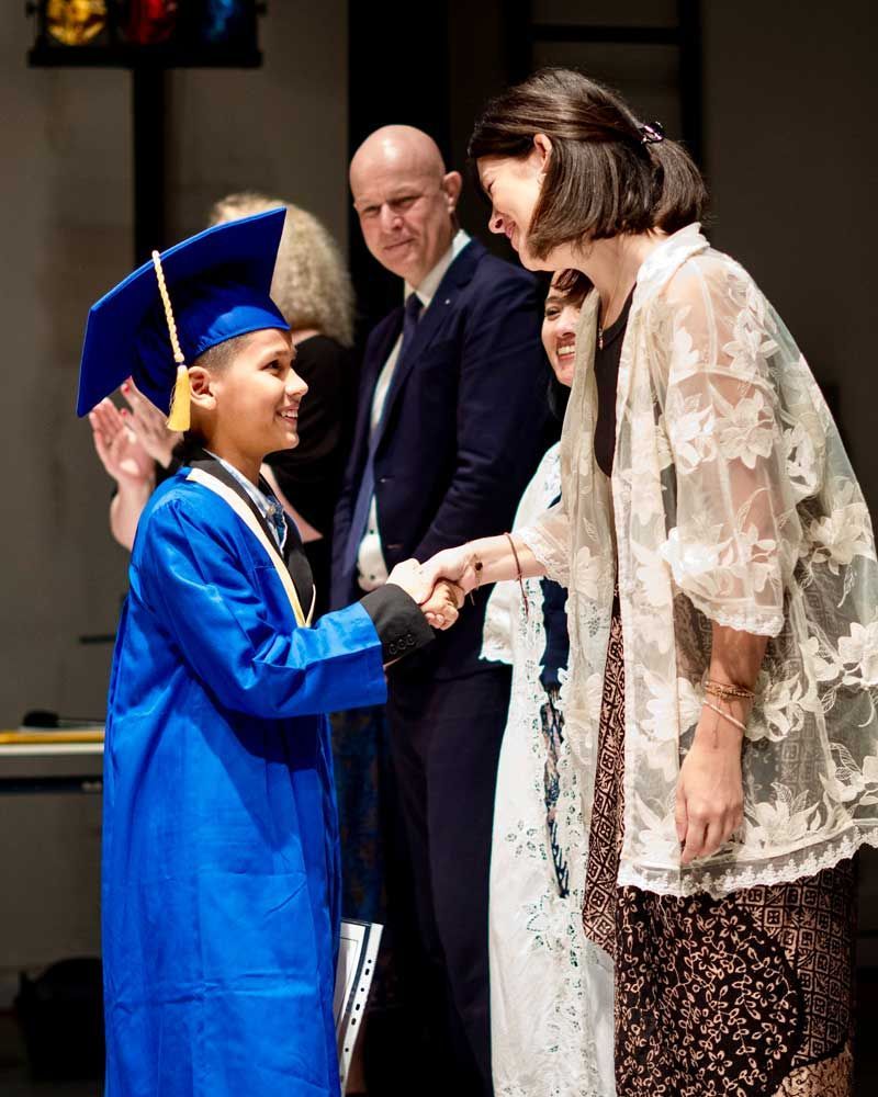 A boy in a blue graduation cap and gown shakes hands with a woman
