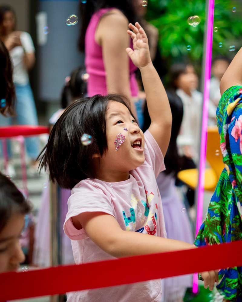 A little girl is playing with soap bubbles in a crowded area.