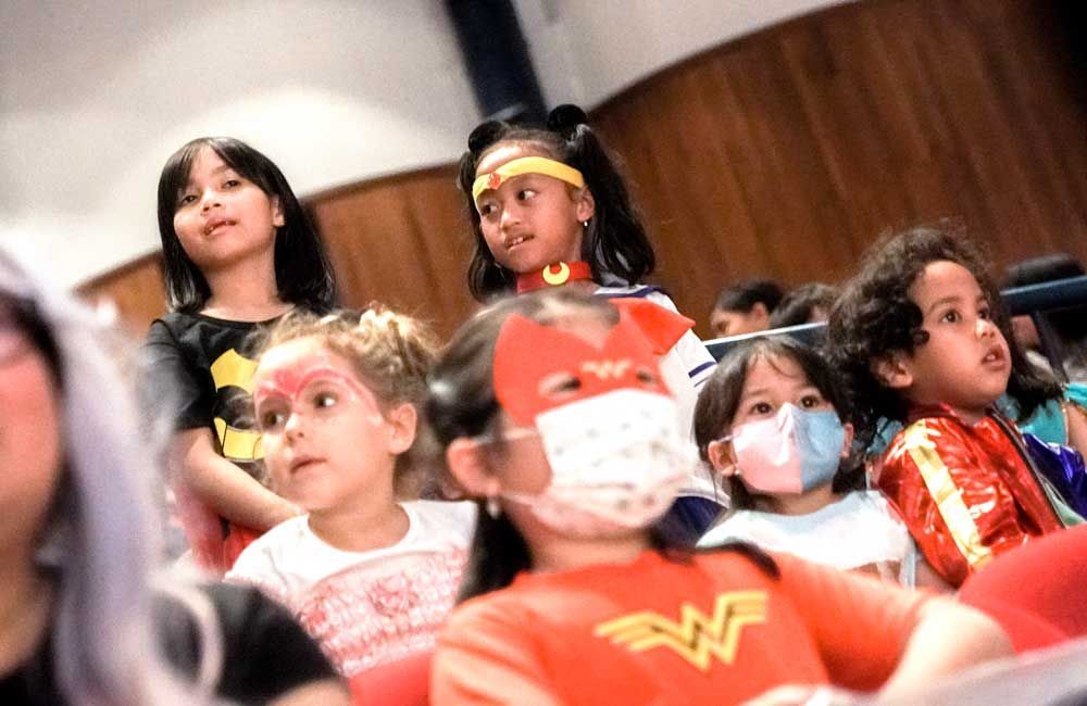 A group of children wearing masks and costumes are sitting in a theater.