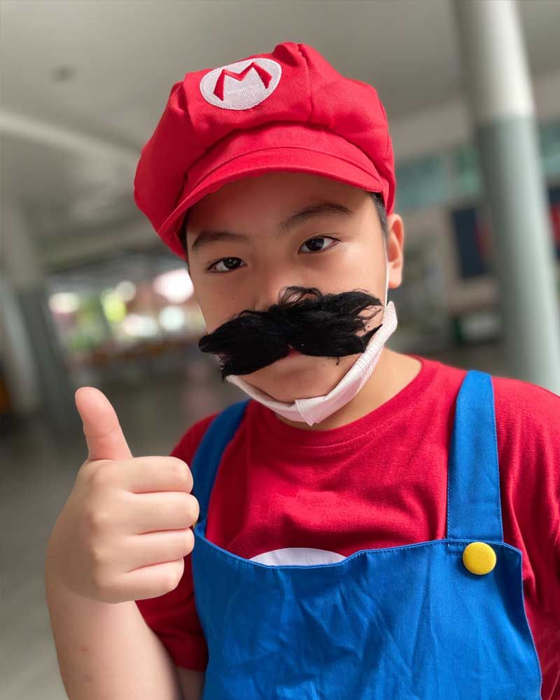 A young boy dressed as mario is giving a thumbs up