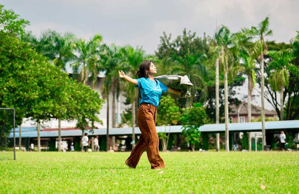 A woman is standing in a grassy field holding a book.