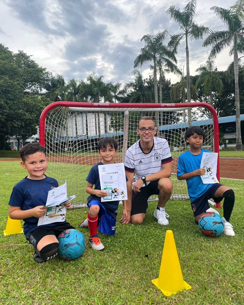 A group of young boys are sitting on the grass with soccer balls and cones.