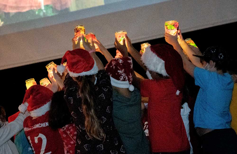 A group of children wearing santa hats are holding up candles.
