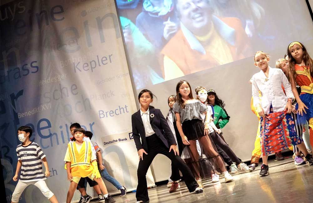 A group of children are dancing on a stage in front of a large screen.
