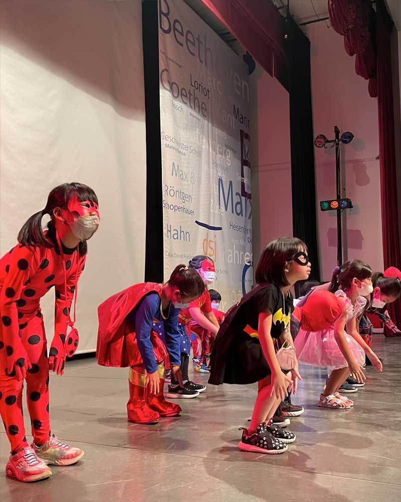 A group of children dressed in superhero costumes are standing on a stage.