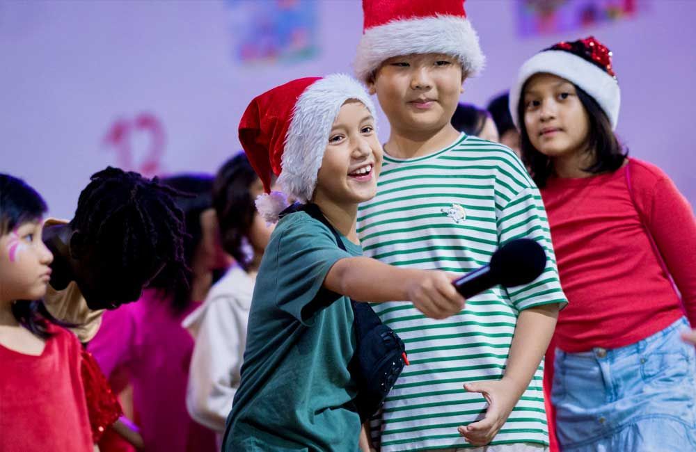 A group of children are wearing santa hats and holding microphones.