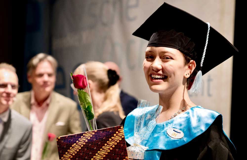 A woman in a graduation cap and gown is holding a rose