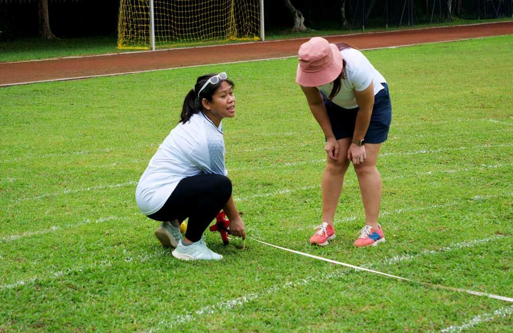 Two women are kneeling on a soccer field and measuring a line.