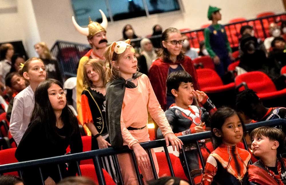 A group of children dressed in costumes are sitting in a stadium.
