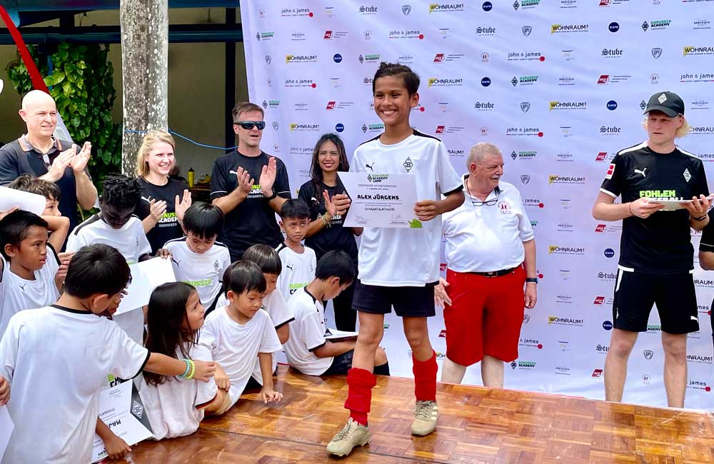 A boy is holding a certificate in front of a group of children.