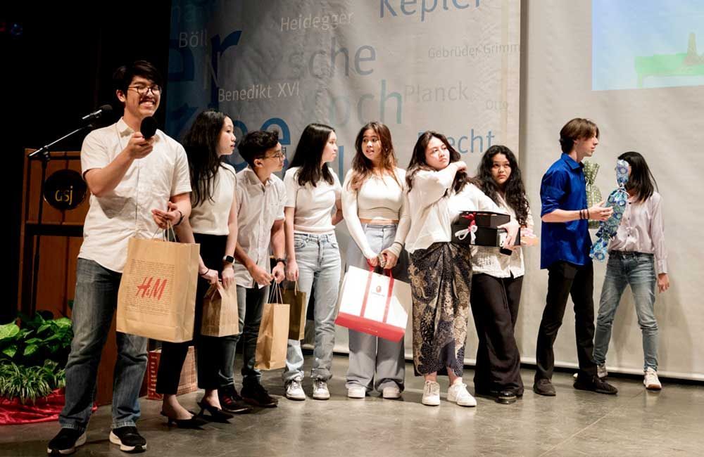 A group of young people are standing on a stage holding bags.