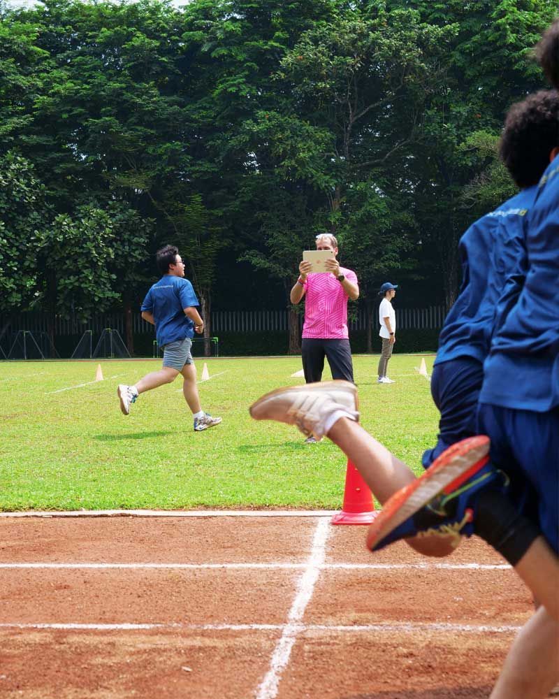 A man in a pink shirt is taking a picture of people running on a track.