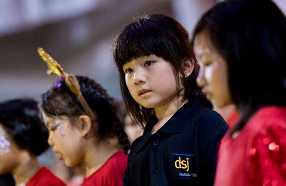 A group of young girls are standing in a line and one of them is wearing a dsj shirt.
