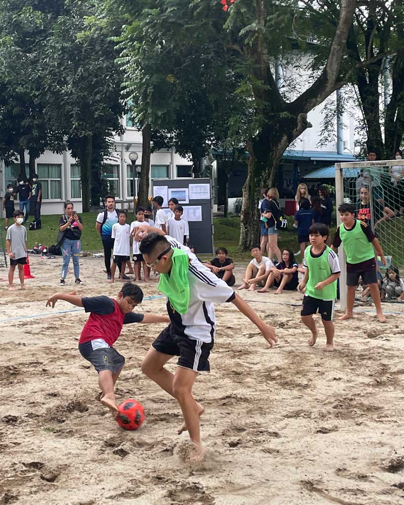 A group of children are playing soccer on a sandy beach.
