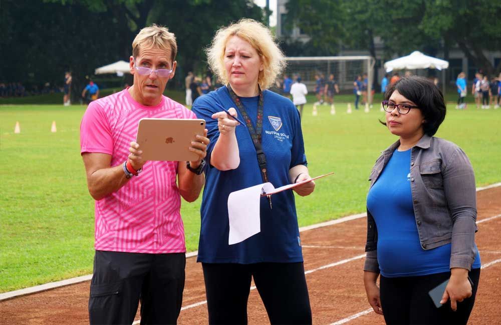 A man and two women are standing on a track looking at a tablet.