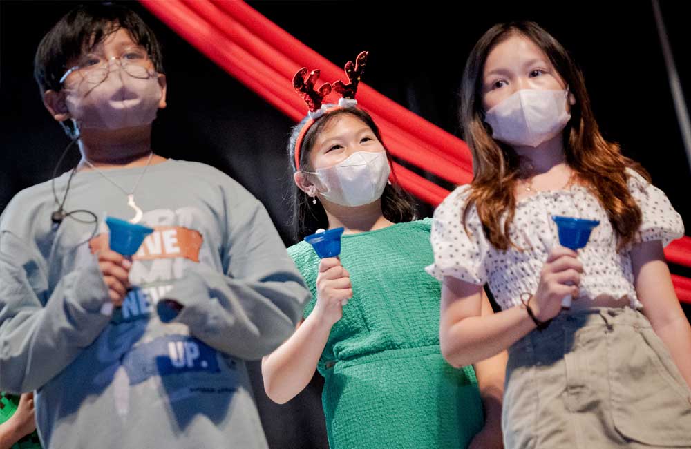 A group of children wearing face masks are holding bells.
