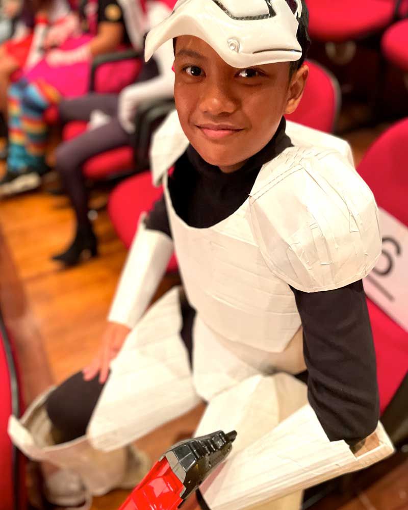 A young boy in a storm trooper costume is sitting in a row of red chairs.