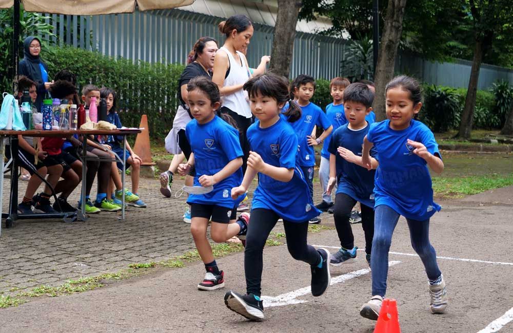 A group of children in blue shirts are running on a track.