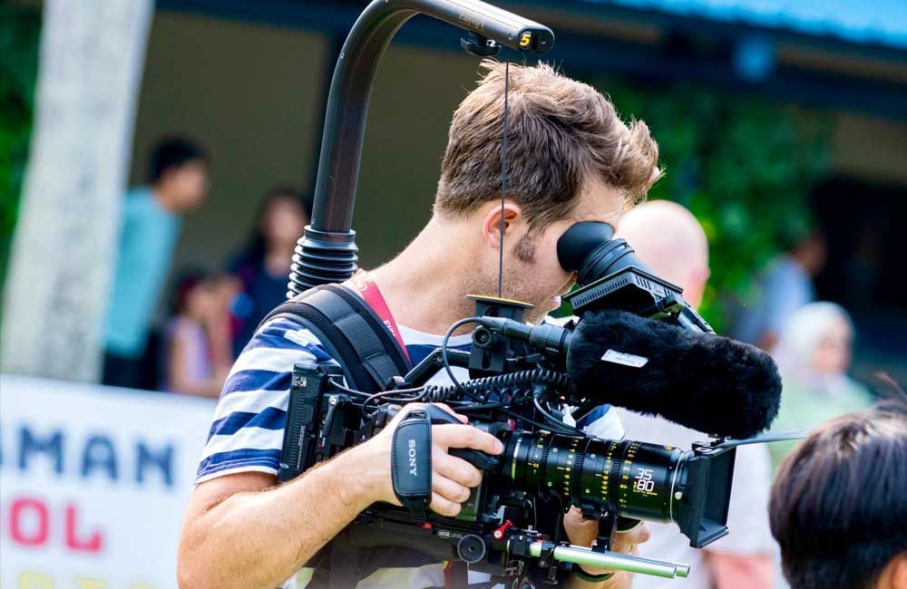 A man is holding a camera in front of a sign that says man ol