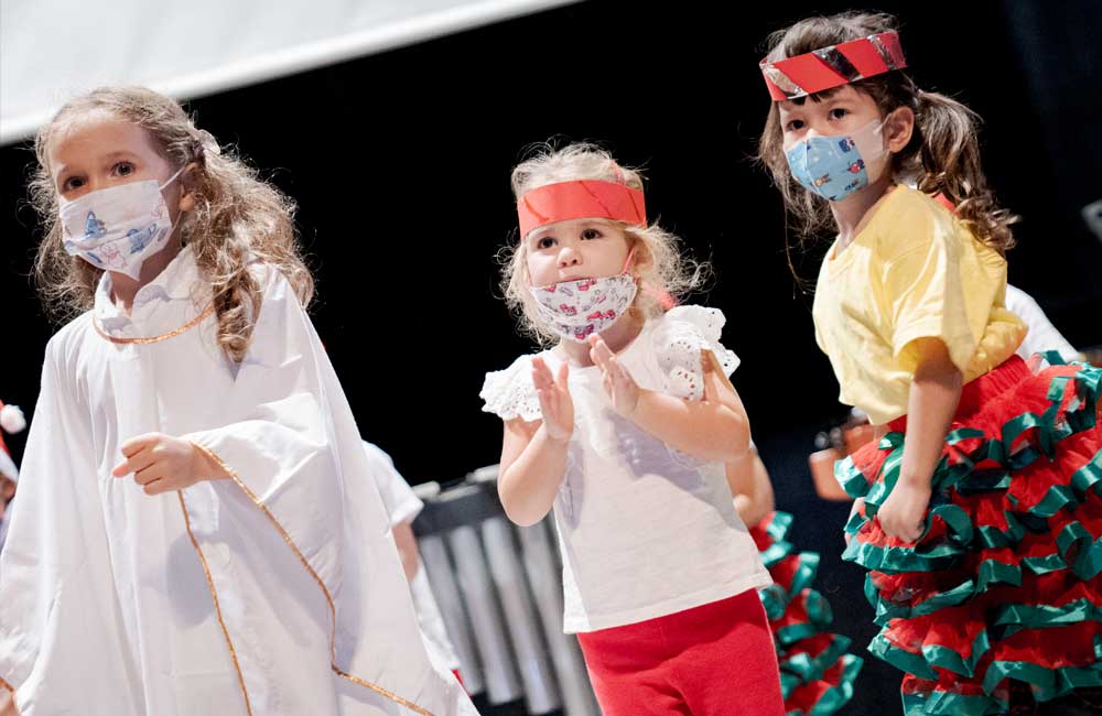 Three little girls wearing face masks are dancing on a stage.