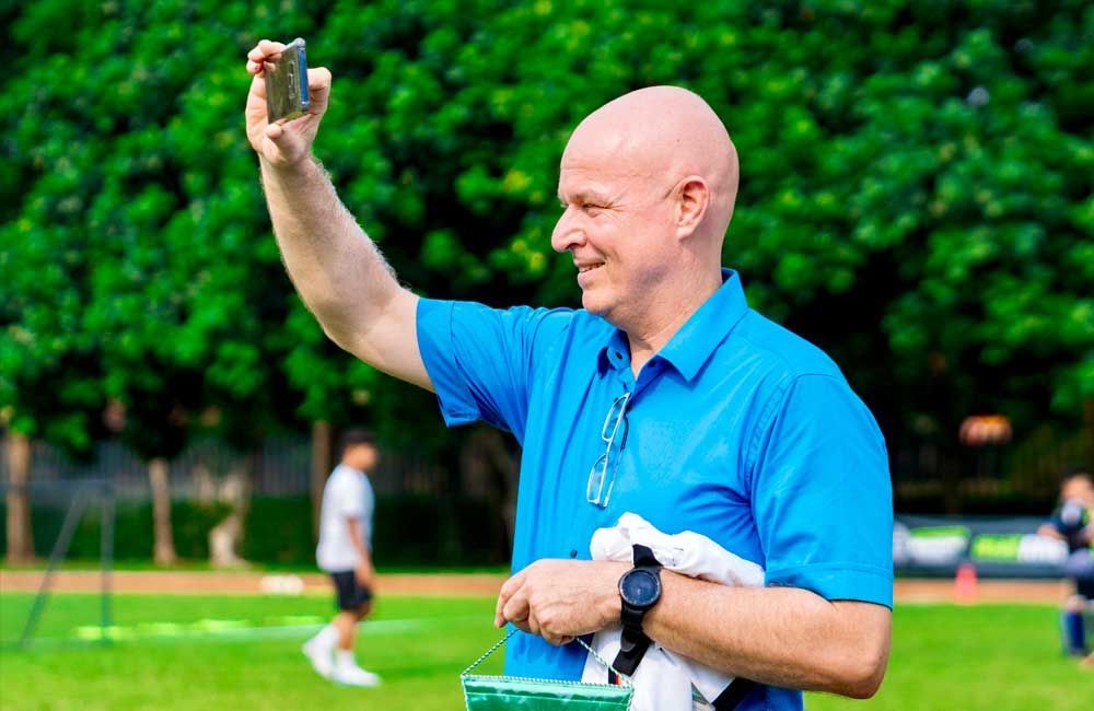 A man in a blue shirt is taking a selfie on a soccer field.