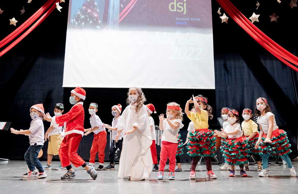 A group of children are dancing on a stage in front of a large screen.