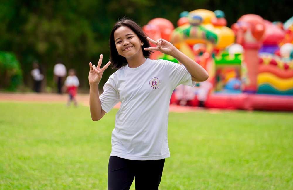 A young girl is standing in a field giving a peace sign.