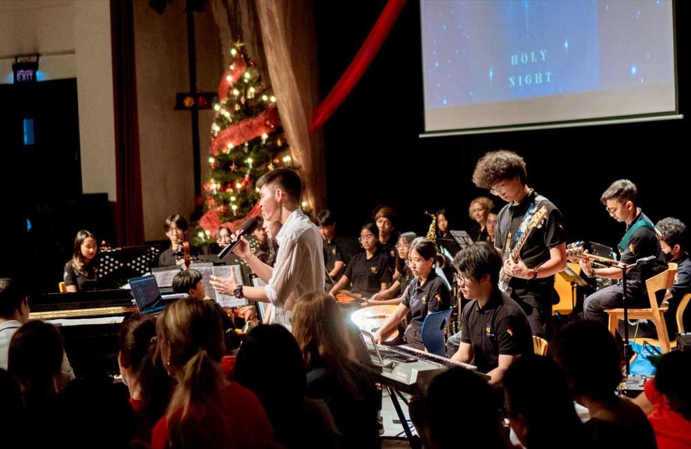 A group of people are playing instruments on a stage in front of a christmas tree.
