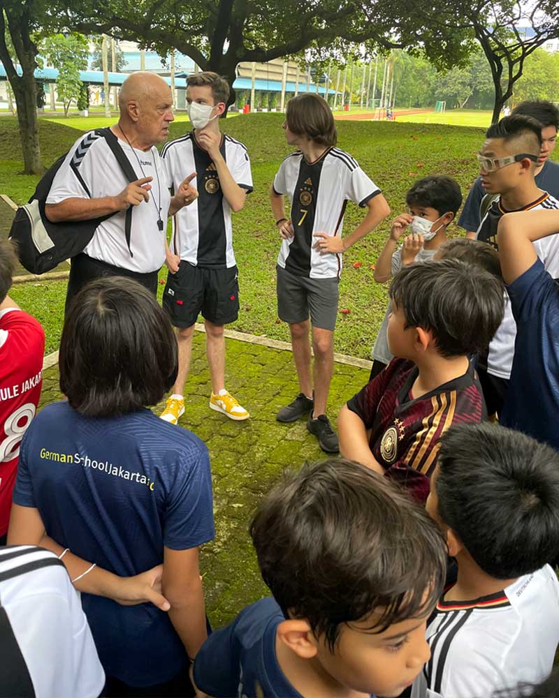 A man wearing a mask is talking to a group of young boys.