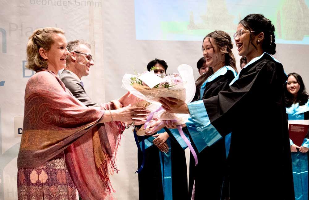 A woman is giving a bouquet of flowers to a graduate.