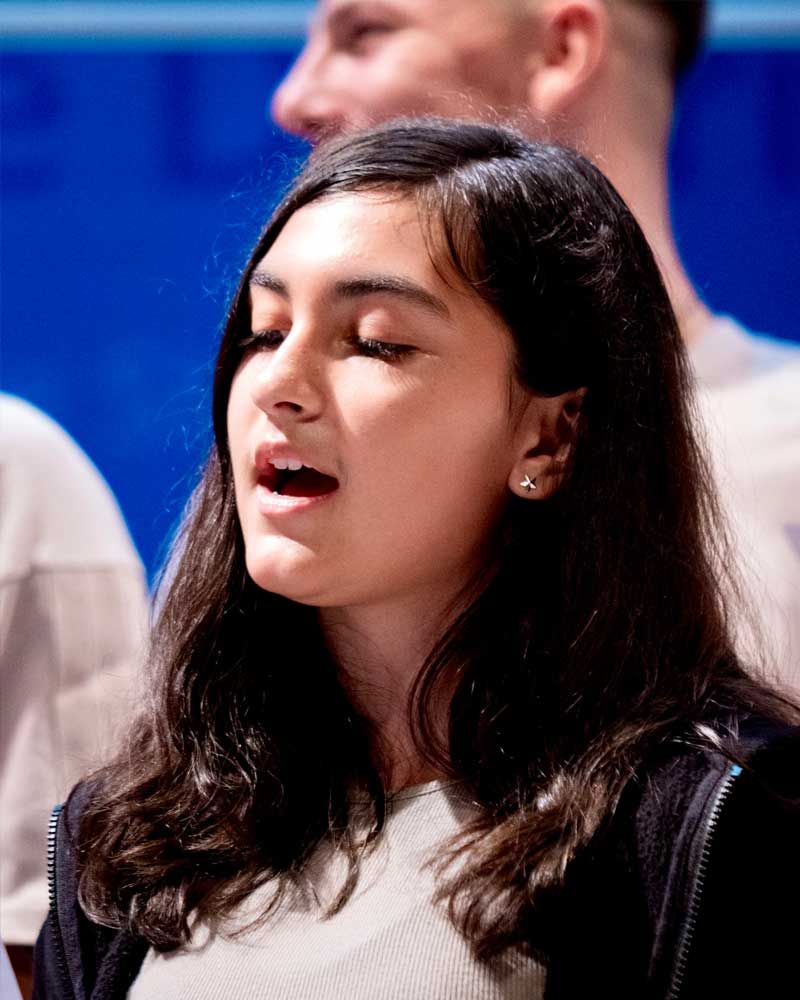 A woman is singing in a choir with her eyes closed.
