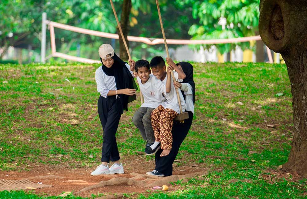 A woman and two children are sitting on a swing in a park.