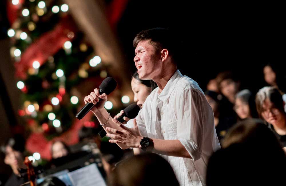 A man is singing into a microphone in front of a christmas tree.