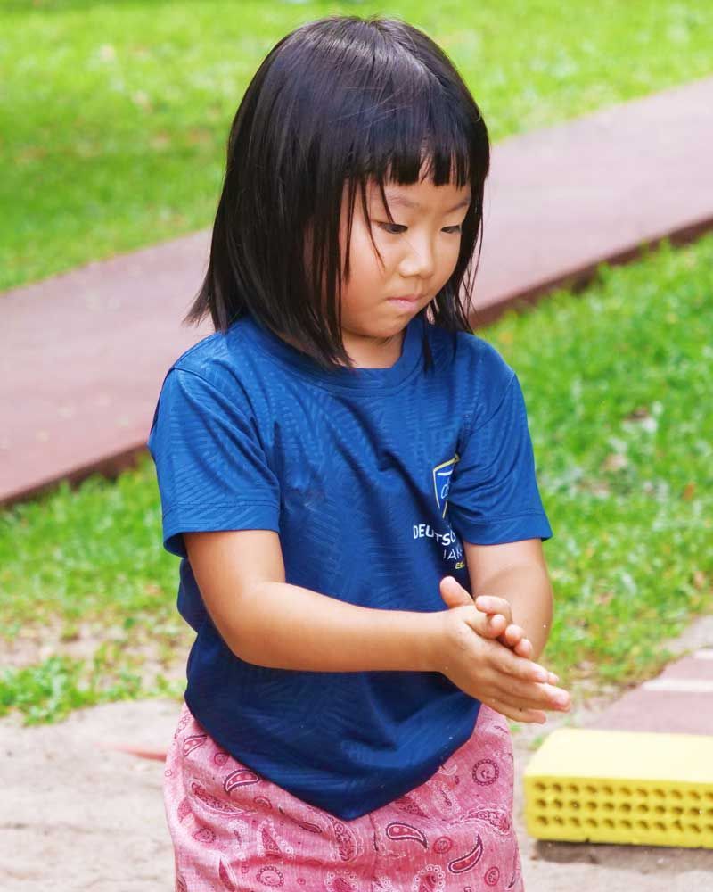 A little girl in a blue shirt is washing her hands