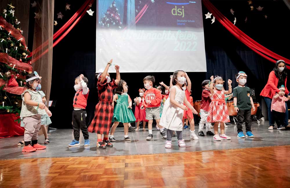A group of children are dancing on a stage in front of a projector screen.
