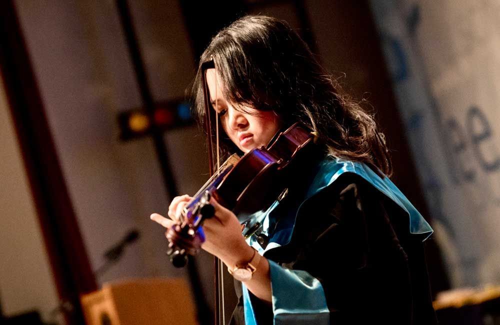 A woman in a graduation cap and gown is playing a violin.
